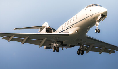 Private jet descending, landing gear extended, gleaming metallic body against azure sky background
