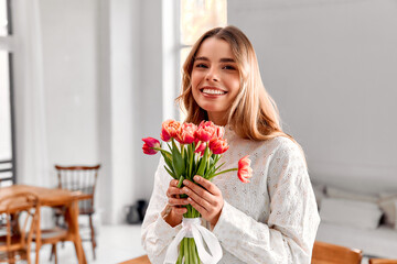 Smiling woman with tulip bouquet. A cheerful young woman in a white blouse holds a bouquet of red...
