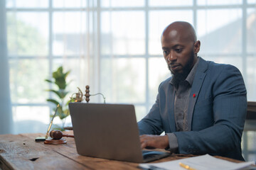 Focused african american lawyer is working on a laptop in his office with a gavel and scales of...