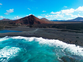 Aerial View of a Volcanic Coastline with Black Sand Beach, and Blue Ocean Waves