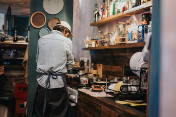 A chef prepares food in a professionally equipped kitchen with rustic decor elements. The setting portrays a charming and warm atmosphere, featuring creatively displayed shelves with various cooking