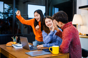 Three Asian young adult students sit around the kitchen table, attending online class on tablet. They engage in video conferencing, discussing lessons, taking notes, digital learning experience.