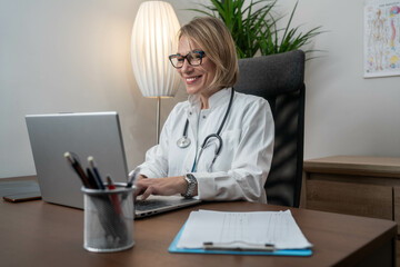 Female mature doctor with laptop working at the office desk.