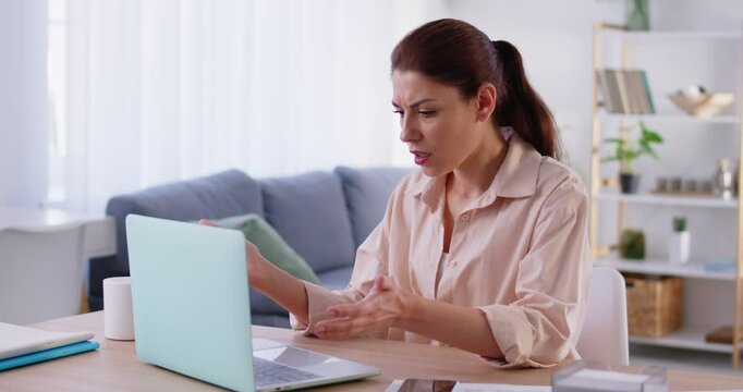 Frustrated angry young woman sitting at desk, having problem due to computer error, losing important data. Desperate girl looking at laptop screen shocked by gadget breakdown or operational problems.