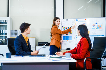 Three Asian business professionals gather in boardroom for annual meeting, discussing strategic goals, future projections while proposing ideas, engaging in decision-making for corporate growth.