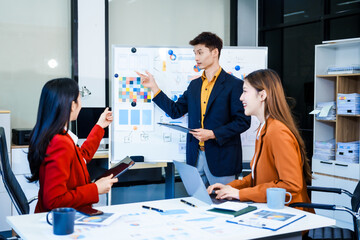 Three Asian business professionals gather in boardroom for annual meeting, discussing strategic goals, future projections while proposing ideas, engaging in decision-making for corporate growth.