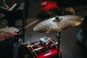 A detailed view of a drummer with stick striking a cymbal, part of a dynamic band rehearsal. The scene captures the energy and precision of music creation in a casual setting.