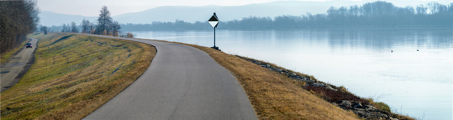 Panorama with a road on a dam along  the river Danube and a navigation sign for the location of the fairway on a cloudy winter day, Austria