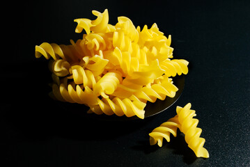 raw spiral shaped pasta (Fusilli) laid out on a black surface ready to cook