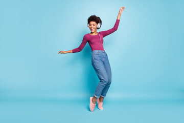 Fototapeta premium Full body photo of cheerful funny mulatto girl have free time listen music on her headset dance sing enjoy wear stylish green pullover denim jeans sneakers isolated over blue color background