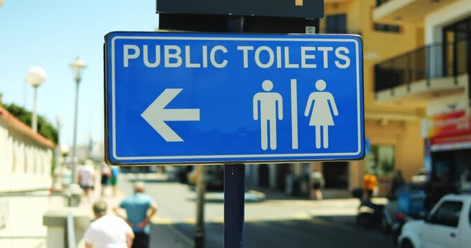 Directional metal plaque indicating Public Toilets location on busy street. Arrow on information board directing to ladies and gentlemen restrooms