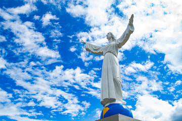 Estatua blanca de Cristo Jesús con manos alzadas parado sobre el  planeta en campo santo Yungay Perú con fondo de cielo azul y nubes © JOSE