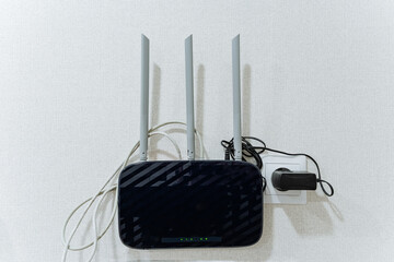 A wireless router is placed on a clean white wall right next to an electrical charger, which is...