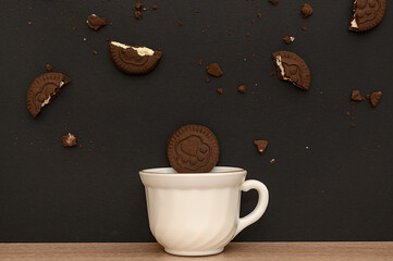 White cup with brown cookies, on a black background. Delicious breakfast.