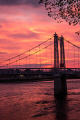 A dramatic sunset with the silhouette  of a pedestrian bridge crossing the River Ness, flowing through the City of Inverness, Scotland