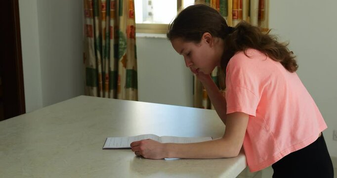 Sedulous brunette studies notes attentively trying to memorize hand gestures. Long-haired young woman leans over table concentrating on jottings