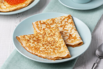 Savory crepes filled with fresh orange fish roe served on a light blue plate at a cozy breakfast table