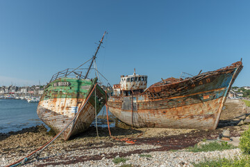 A rusty boat is sitting on the shore next to a large concrete post