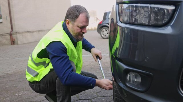 Melle, Germany, 02.20.2025. A man unscrews nuts with a wheel wrench. He holds the tool with both hands. The car is on a level surface, raised by a jack. Basic set of tools for changing wheels.