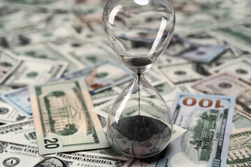 Photo of hourglass and US dollar bills currency. Deadline or economic crisis. Time is money concept