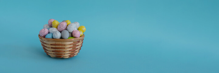 On a blue background, on the left side there is a wicker basket filled with Easter colorful eggs, on the right side there is a place for text, advertising or congratulations. Side view. 