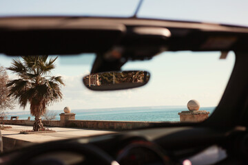 view from a convertible car through the glass onto the beach and the sea coast embankment and palm...