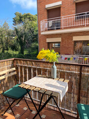 Sunlit balcony with yellow flowers in a vase, outdoor relaxation, cozy urban living, springtime