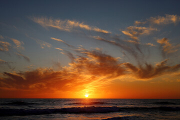 Beautiful golden sunset on the beach over the ocean with feathery clouds