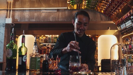 Smart Asian bartender using stirring mixed alcohol syrup into glass with ice for on the rock served...