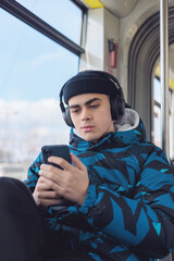 Teenager in public transport wearing headphones, focused on smartphone. Urban commuting, digital...