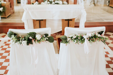 Wedding ceremony in a church with decorated chairs for the bride and groom. Floral wedding decorations at the altar. Sacred vow exchange in an elegant and romantic setting.