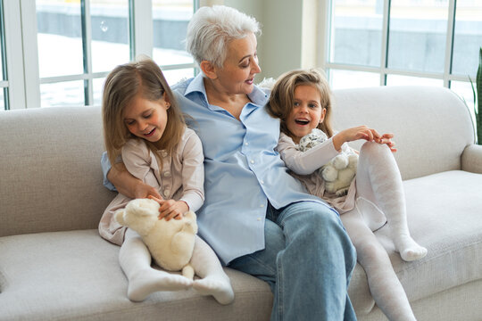 Happy family at home. Two little girls sisters twins grandmother enjoying time together. Good time at home. Grandma granddaughters child kids emotional bonding hugging together. Family generations