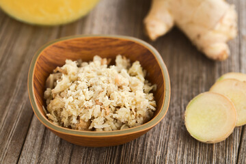 Freshly grated ginger in small bowl with ginger root and slices  in the back (Selective Focus, Focus one third into the bowl)