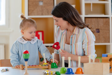 A smiling young woman and a little girl engage in a fun educational activity, playing with musical toys in a bright, cheerful indoor setting