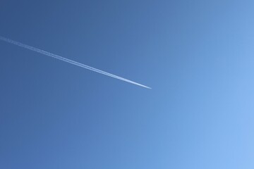 A high-altitude airplane leaves a white contrail across a vast blue sky. The minimalistic composition highlights the beauty of flight and open space