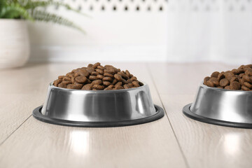 Dry pet food in feeding bowls on floor indoors