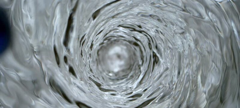 Slow-motion shot of clear fresh water vortex moving in a spiral shape and taking in blue color. Close-up top view