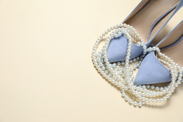 Stylish shoes and pearl necklace on beige background. Space for text