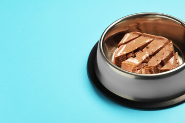 Wet pet food in feeding bowl on light blue background, space for text