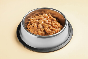 Wet pet food in feeding bowl on pale yellow background