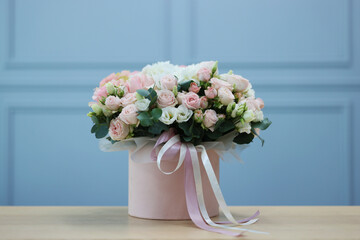 Gift box with bouquet of beautiful flowers and eucalyptus branches on wooden table against light blue wall