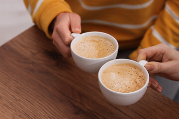 Coffee break. Women with cups of hot drinks at wooden table indoors, closeup