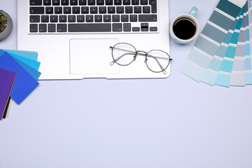 Designer's workplace with color palettes, cup of coffee, glasses and laptop on grey table, flat...