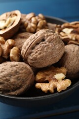 Fresh walnuts in bowl on blue table, closeup