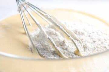 Whisk and bowl of dough, closeup view