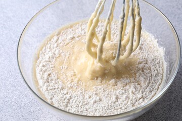 Whisk and bowl of dough on grey table, closeup