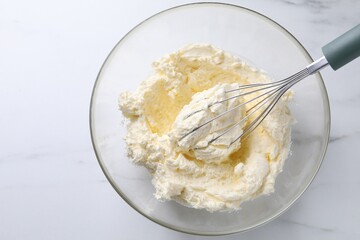 Bowl with whisk and whipped cream on white marble table, top view