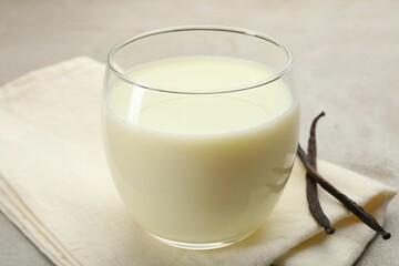 Glass of milk and vanilla pods on light grey table, closeup