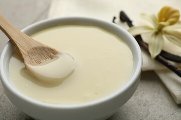 Tasty condensed milk, vanilla pods, flower and spoon on light grey table, closeup