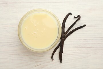 Tasty condensed milk and vanilla pods on white wooden table, flat lay